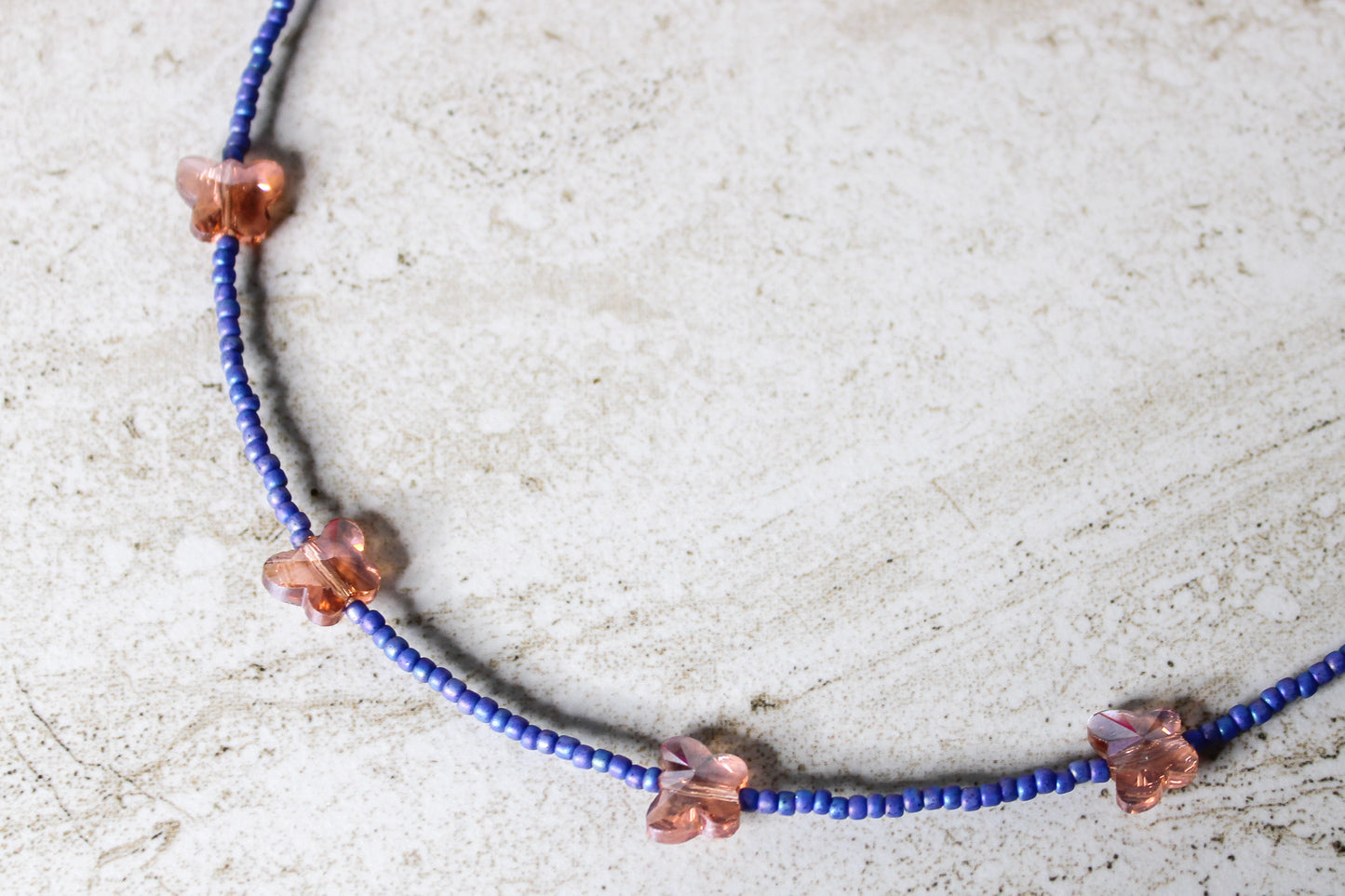 Close-up of the necklace with blue and orange glass beads and the butterfly charm in full detail.