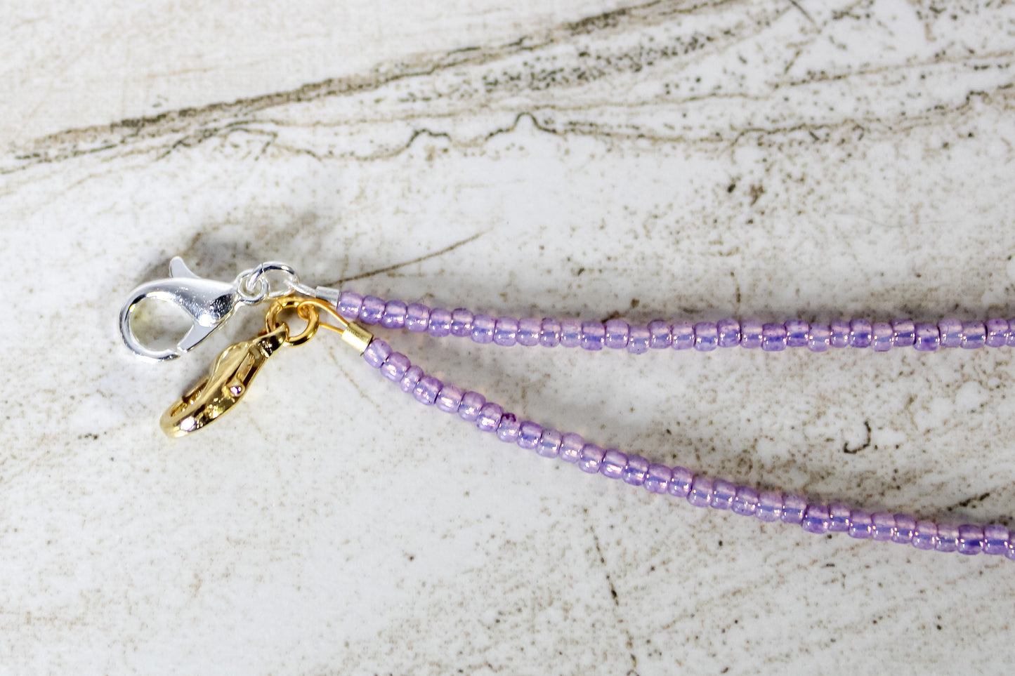A close up of the gold and silver lobster clasps on a purple bracelet.