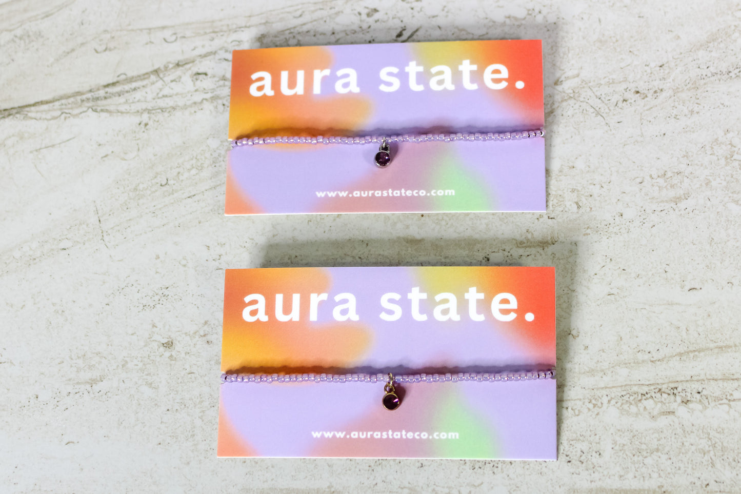 A purple beaded bracelet with an amethyst charm on a rectangular card that says aura state.
