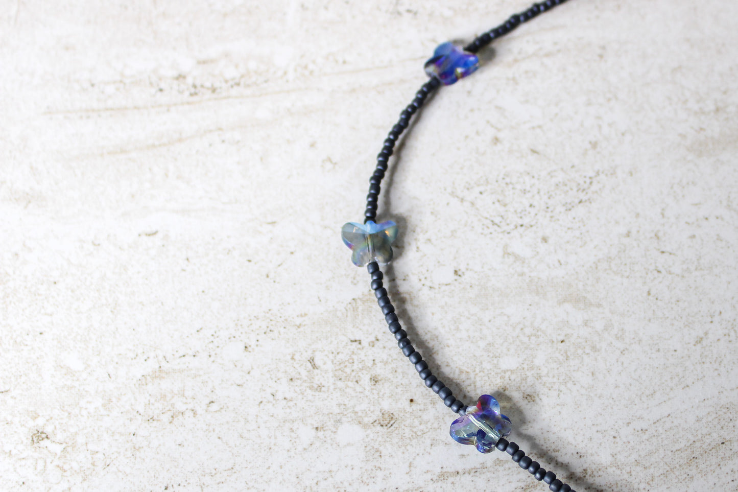 Close-up view of the grey and blue glass beads with the butterfly charm, showcasing the soothing tones and design.