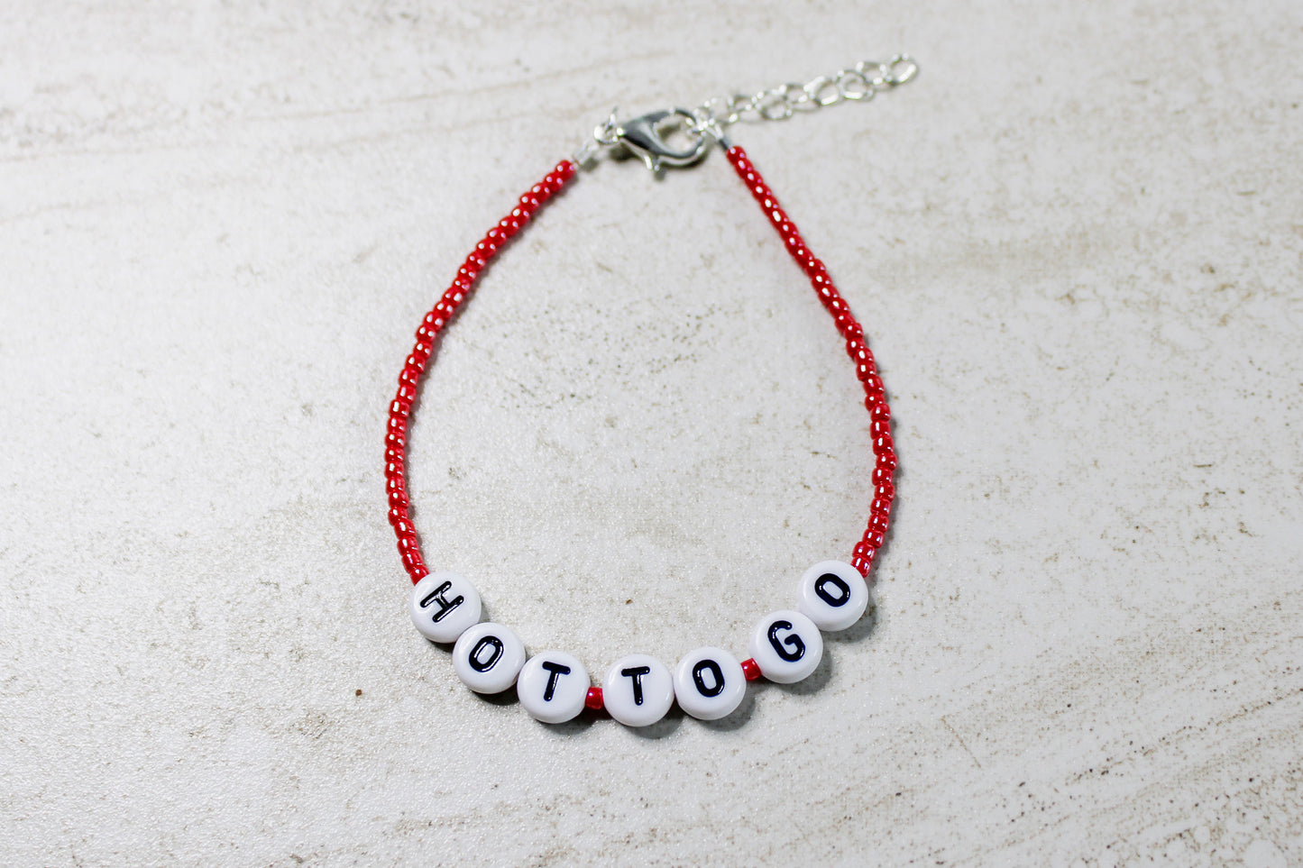 A vibrant red beaded bracelet featuring white letter beads spelling out "Hot to Go," showcasing its bold and playful design.