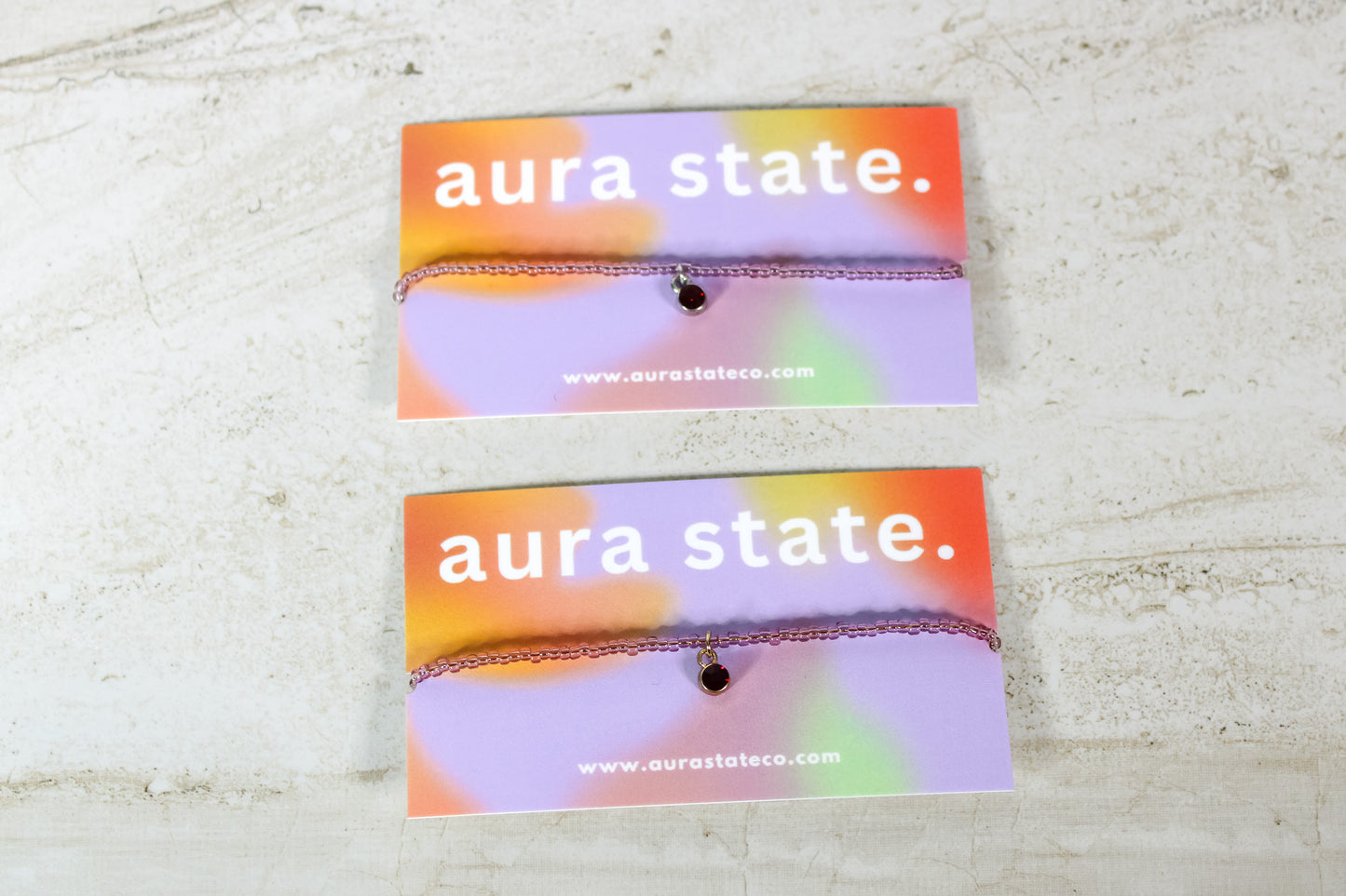 A garnet beaded bracelet with a garnet charm on a rectangular card that says aura state.