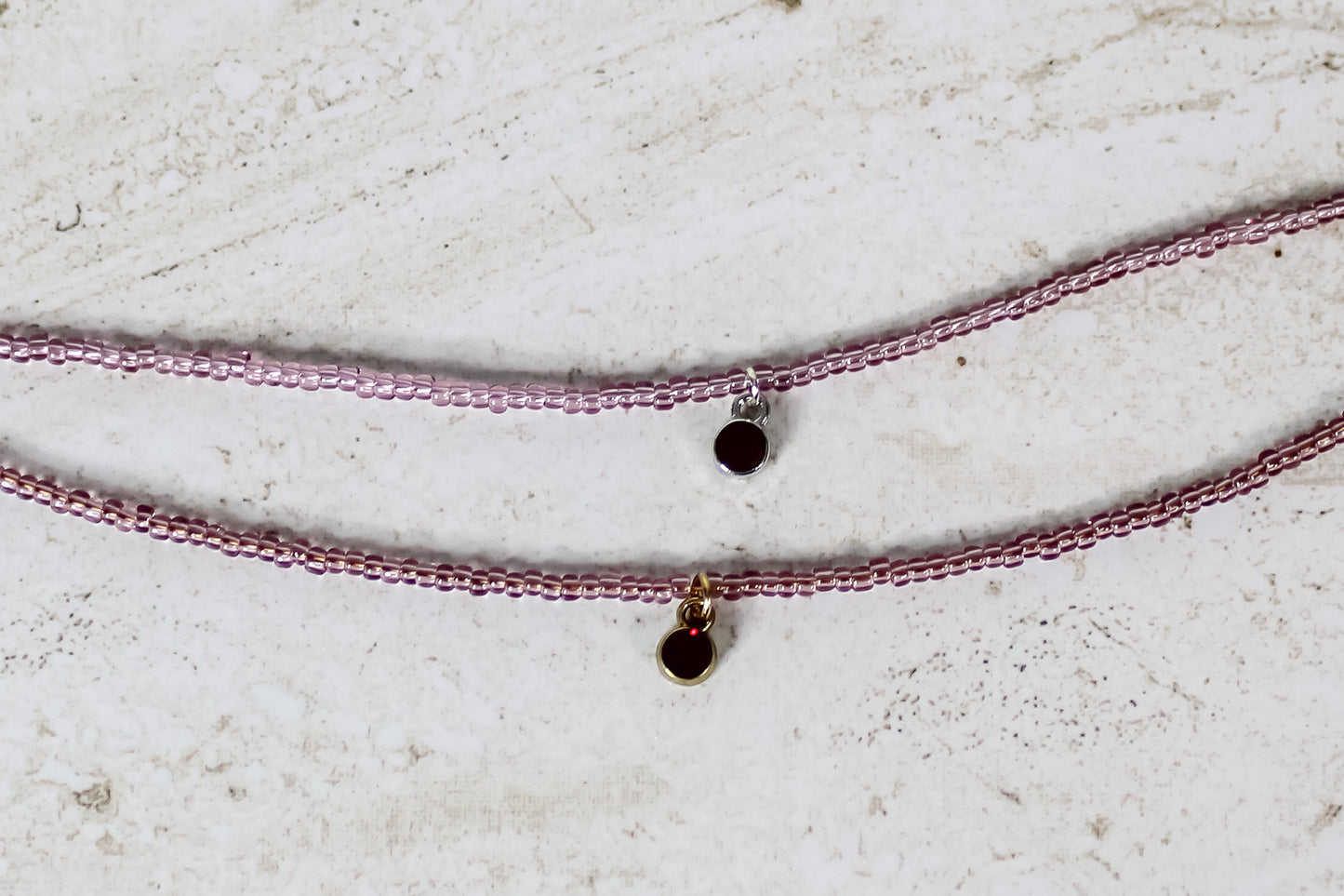 Two bracelets made out of garnet seed beads and either a gold or silver circular garnet cubic zirconia charm.