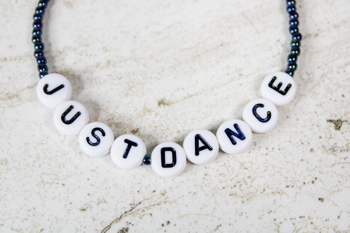Close-up of the Just Dance phrase spelled out in colorful letter beads surrounded by shimmering oil slick seed beads.