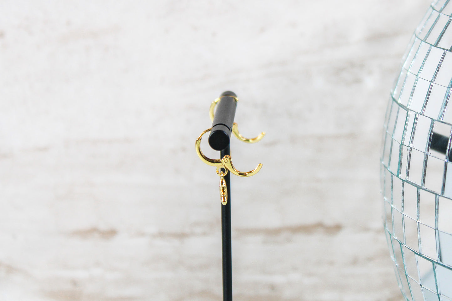 A pair of gold huggie hoop earrings with small north star charms are displayed on a t bar, showing the open clasp of the earrings.