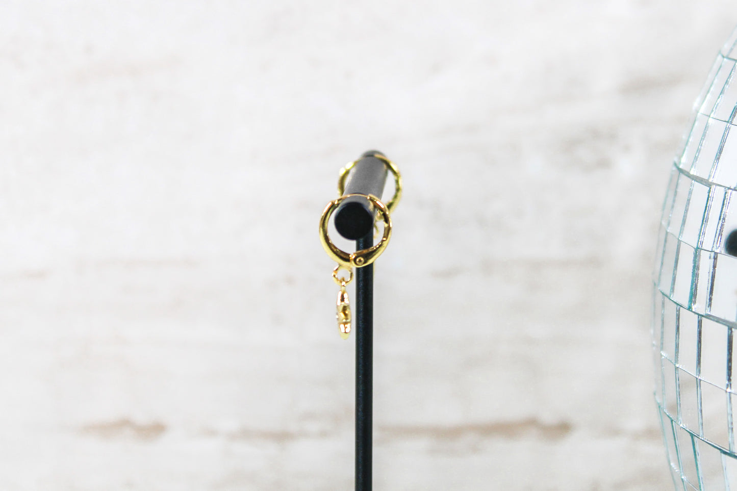 A pair of gold huggie hoop earrings with small north star charms are displayed on a t bar, showing the side of the earrings.
