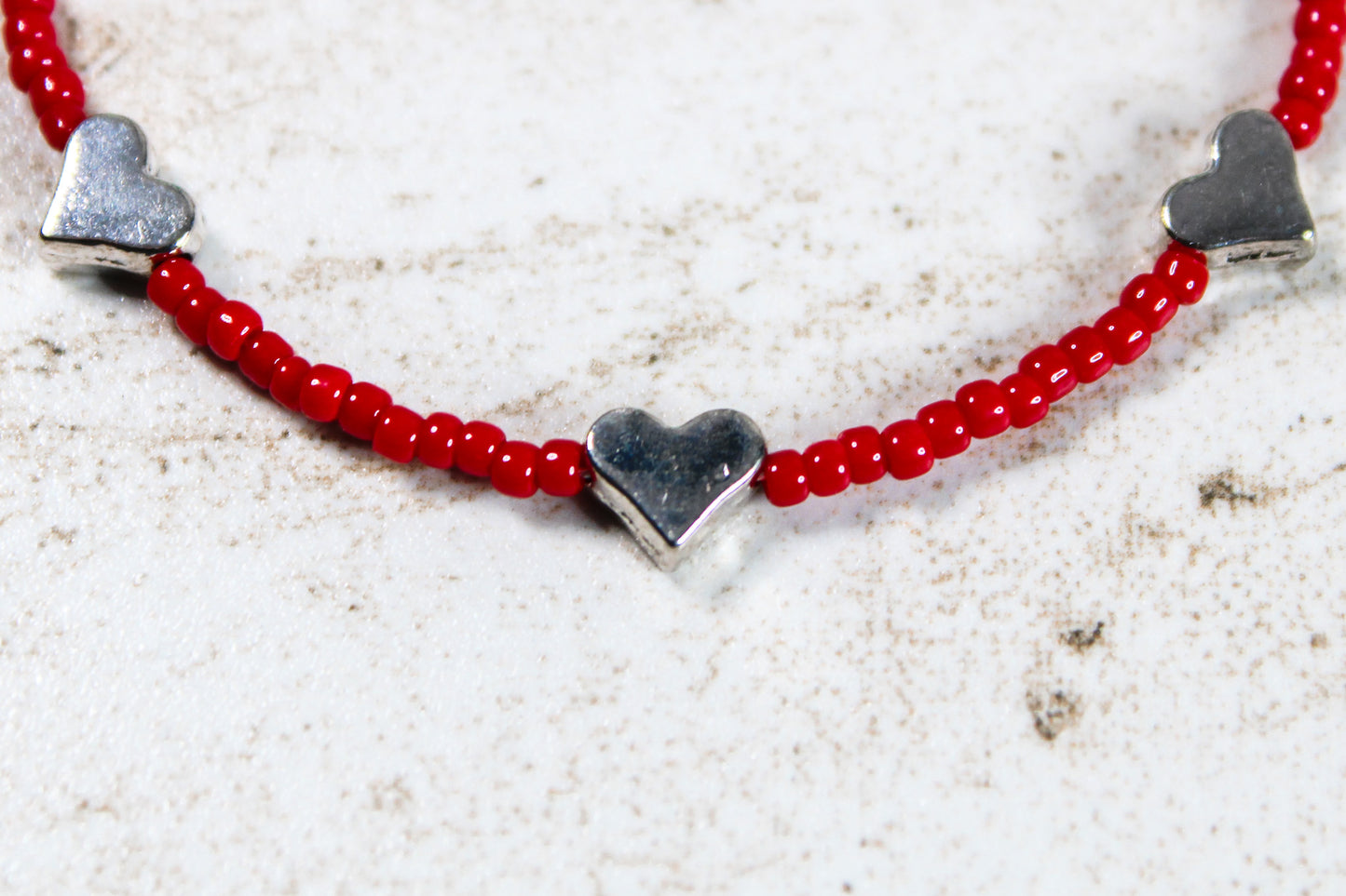 A close up of the red seed beads and silver metal hearts.