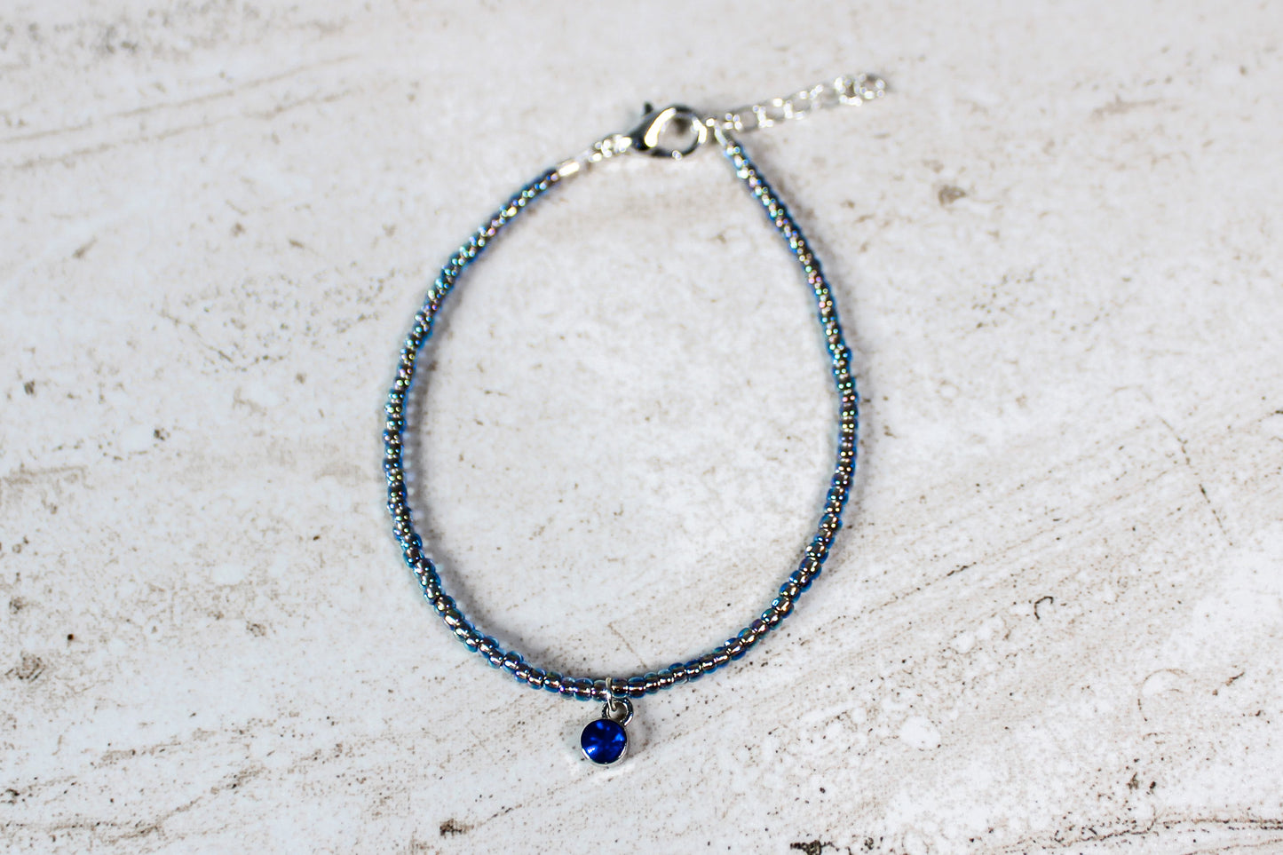 September birthstone bracelet with deep sapphire-colored beads and silver hardware, displayed on a minimal backdrop.