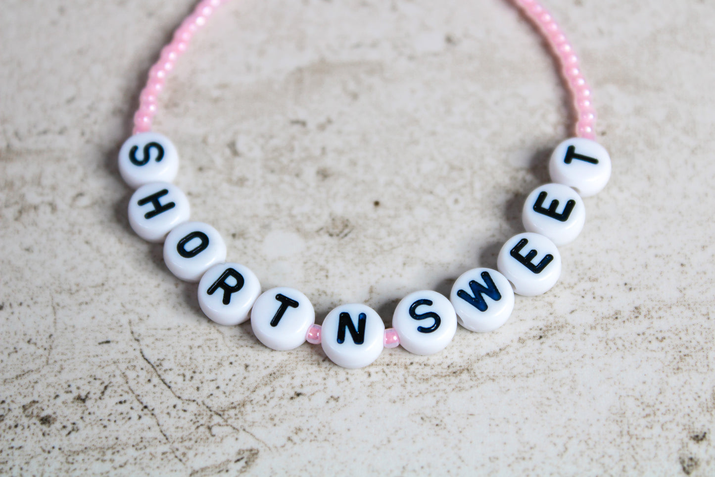 Close-up of the words Short n Sweet spelled in letter beads surrounded by light pink seed beads