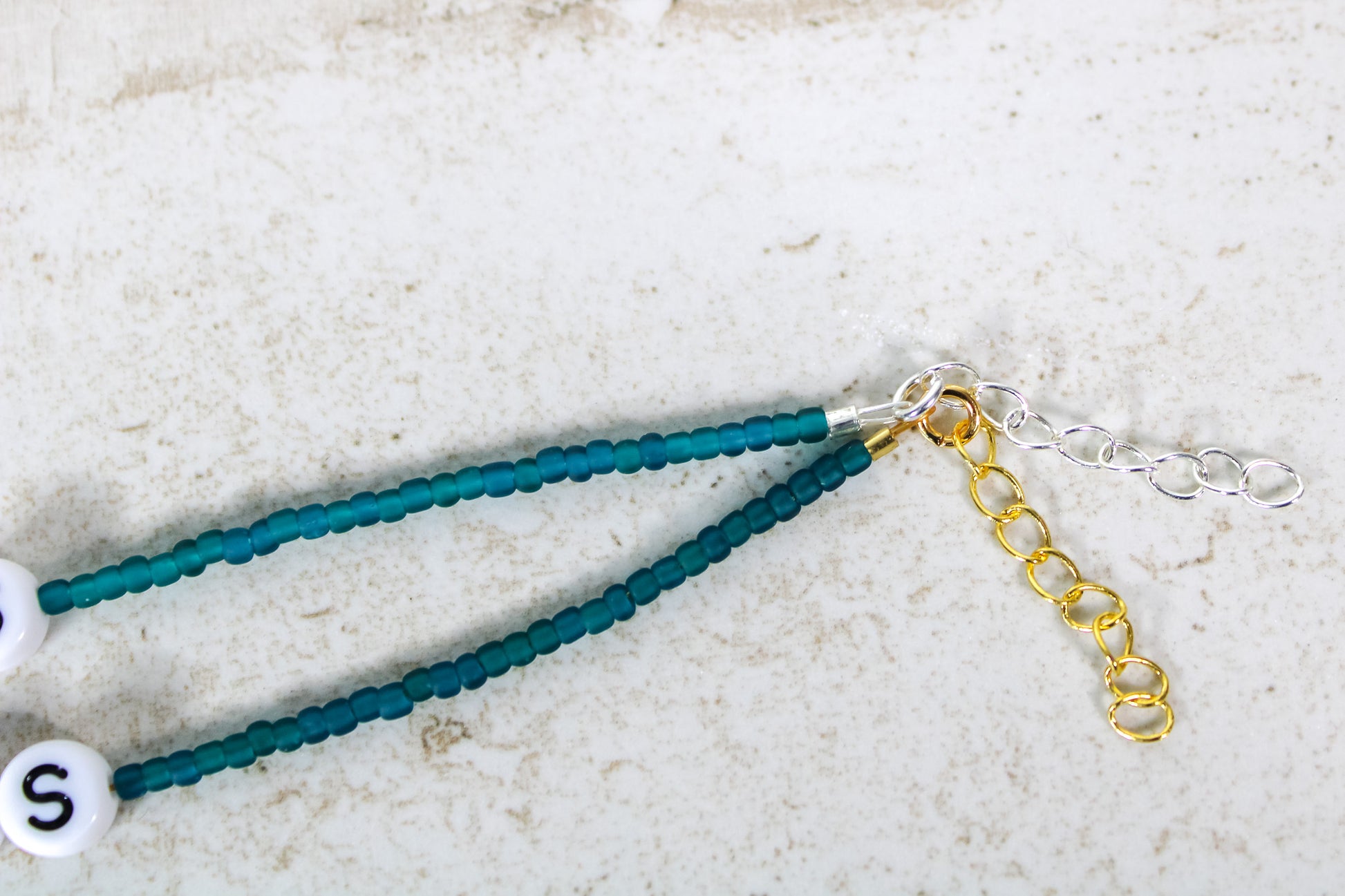 A close up of the gold and silver extender chains on a teal bracelet.