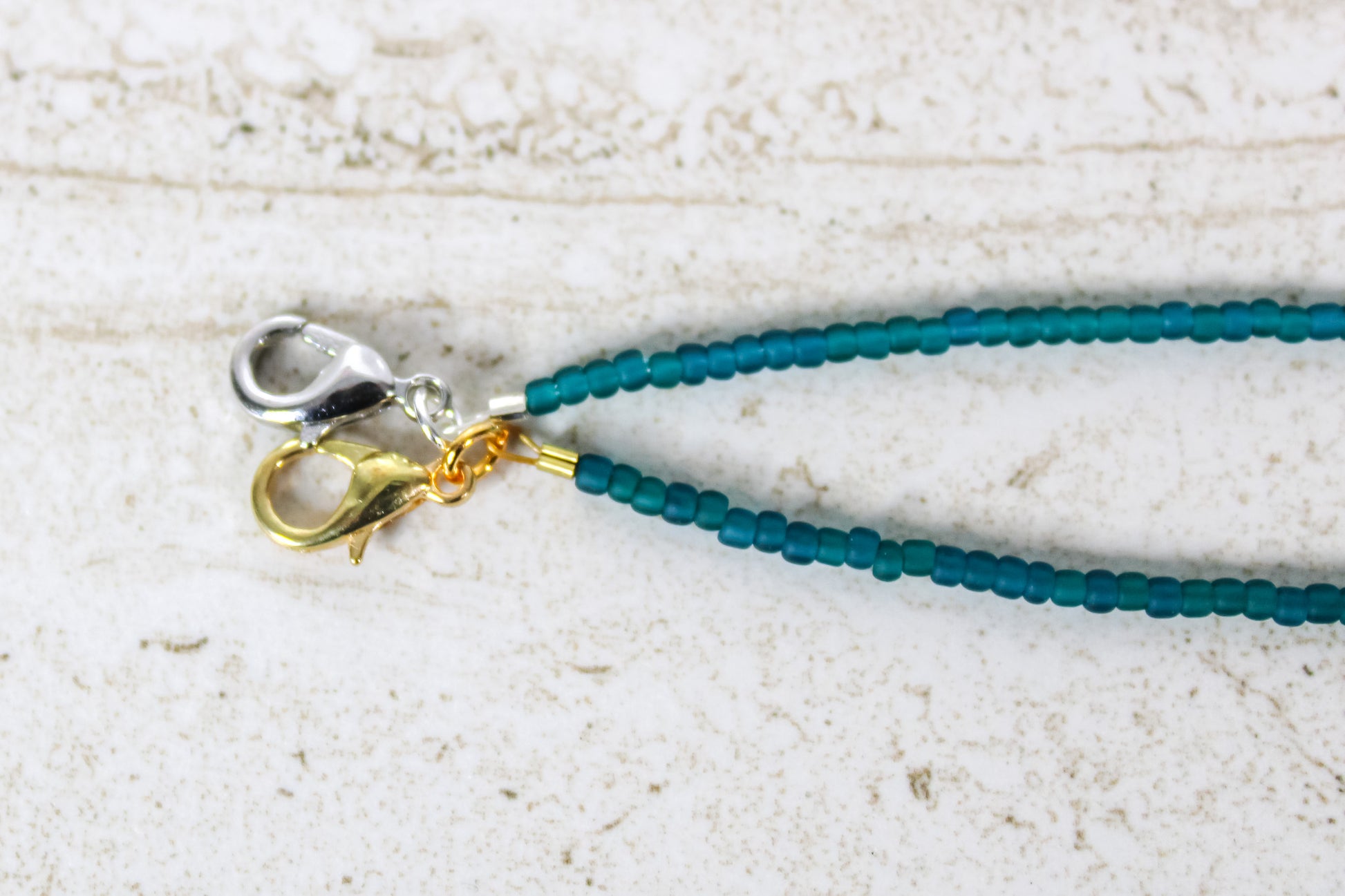 A close up of the gold and silver lobster clasps on a teal bracelet.