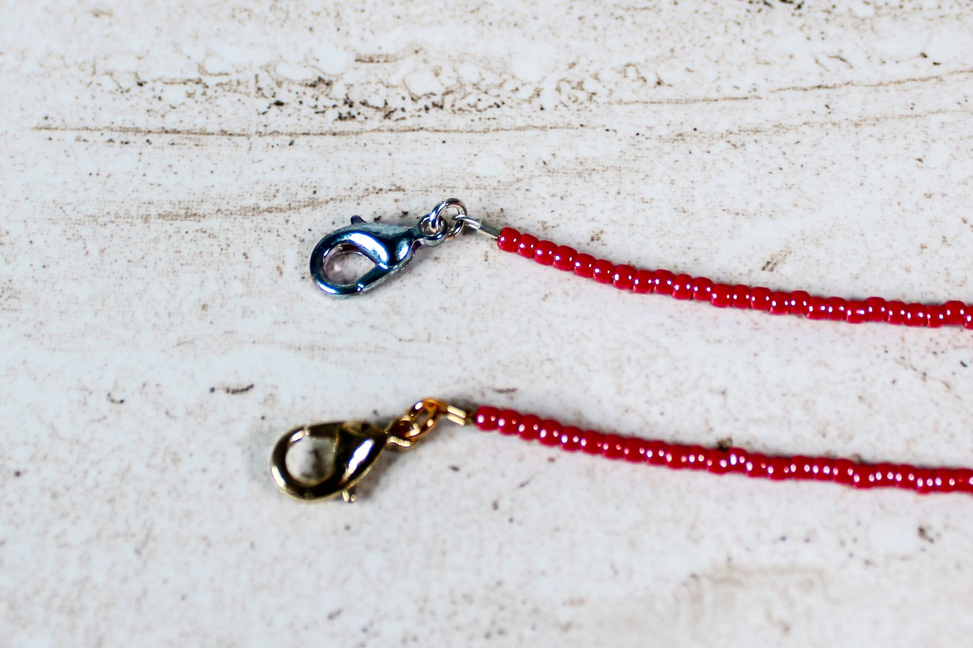 A close up of the gold and silver lobster clasps on a shiny red bracelet.