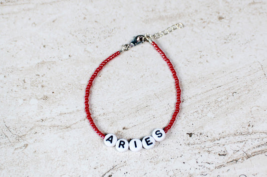 A shiny red colored seed bead bracelet with Aries in round letter beads and silver lobster clasp and extender chain.