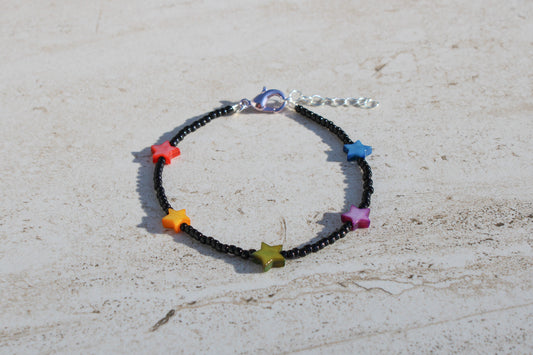 A bracelet made out of black seed beads and red, yellow, green, purple, and blue shell star charms.  Features a silver lobster claw clasp and chain extender.