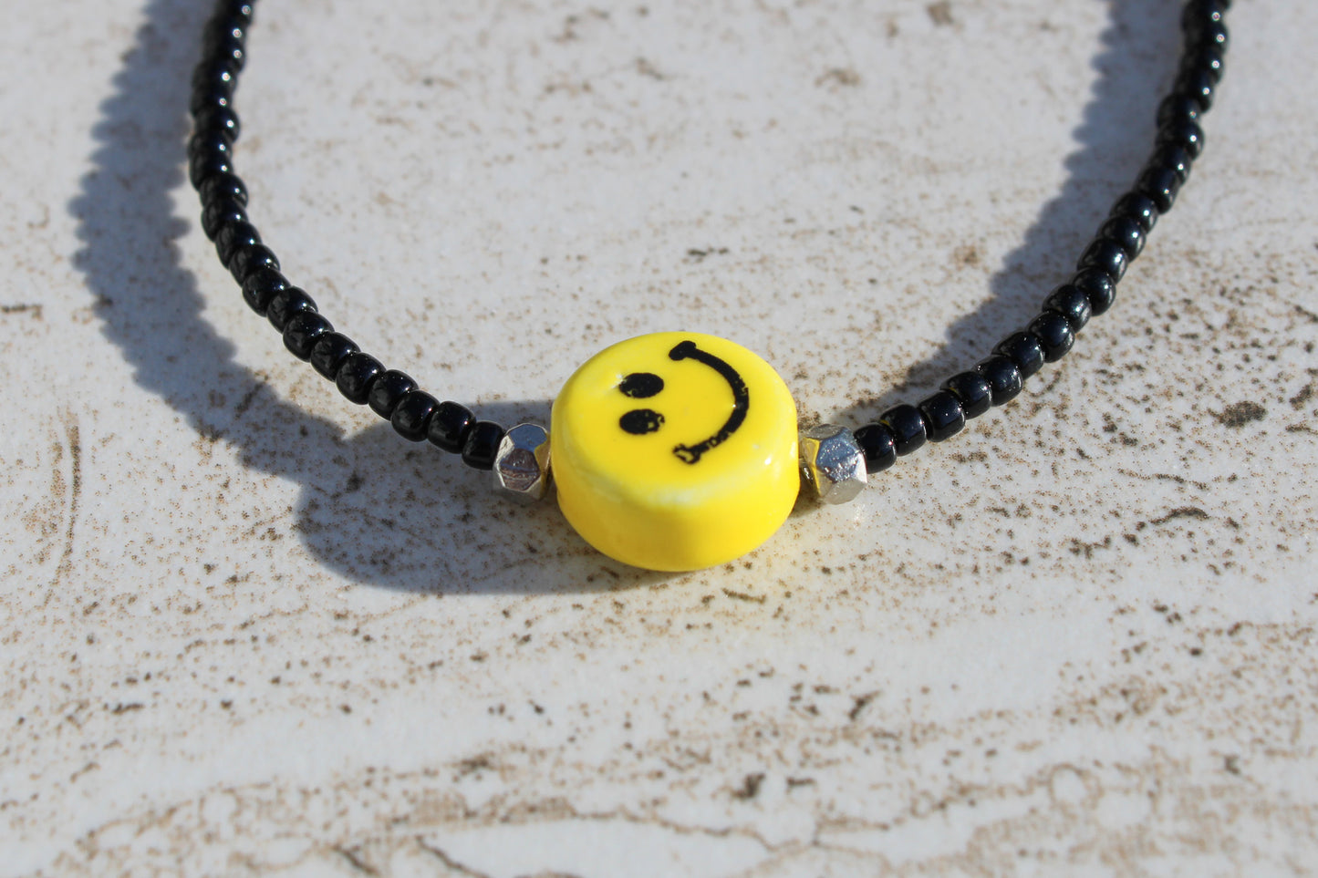 A close up of the yellow smiley face charm supported by a silver bead on each side.