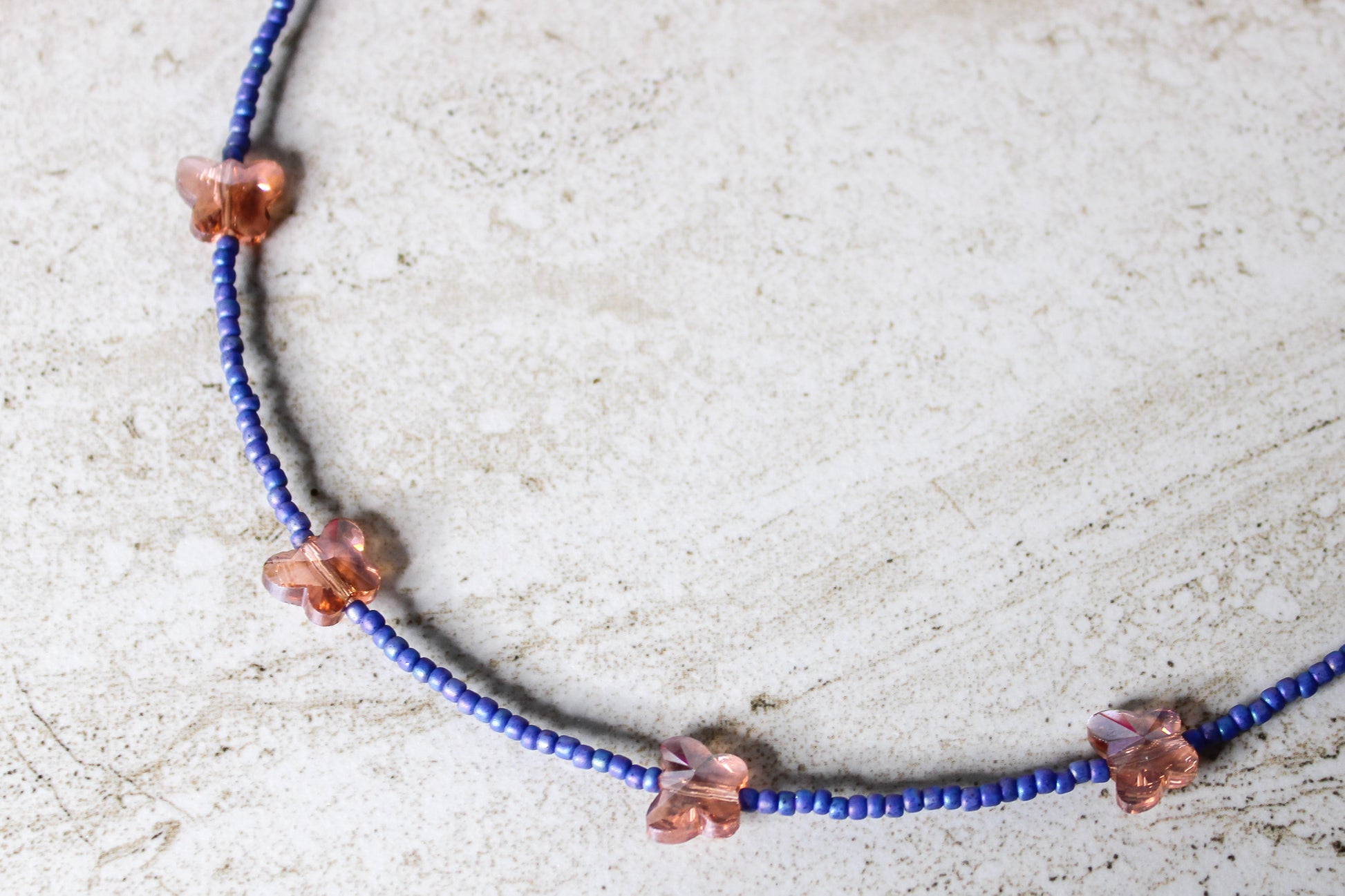 Close-up of the necklace with blue and orange glass beads and the butterfly charm in full detail.