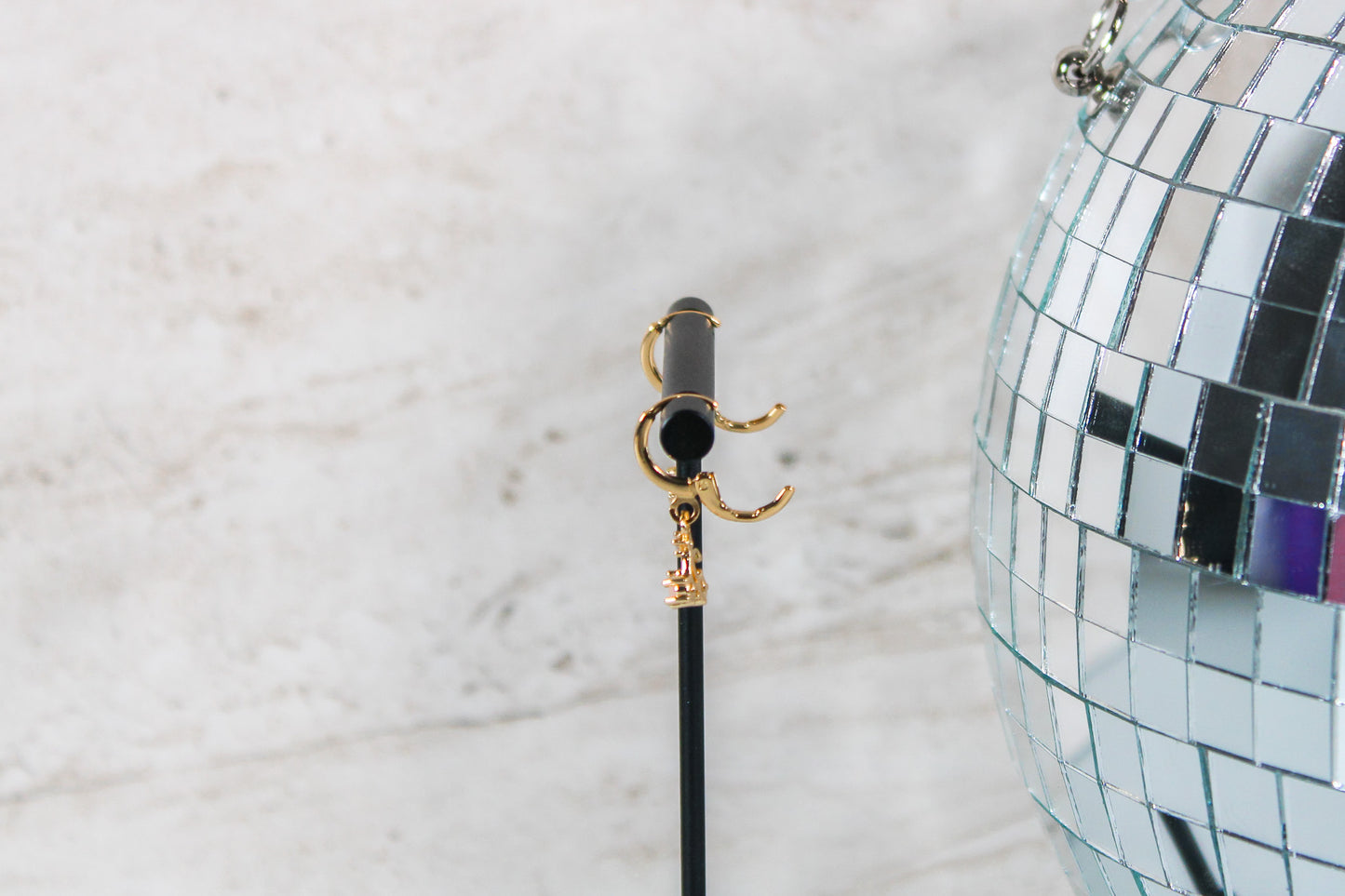 A pair of gold huggie hoop earrings with small cherry charms are displayed on a t bar, showing the open clasp of the earrings.