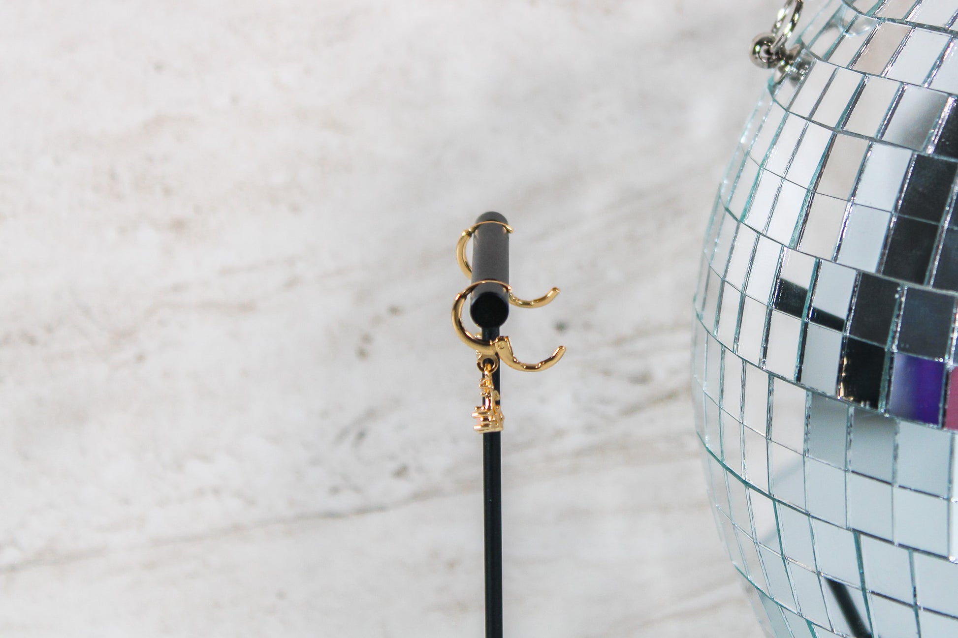 A pair of gold huggie hoop earrings with small cherry charms are displayed on a t bar, showing the open clasp of the earrings.