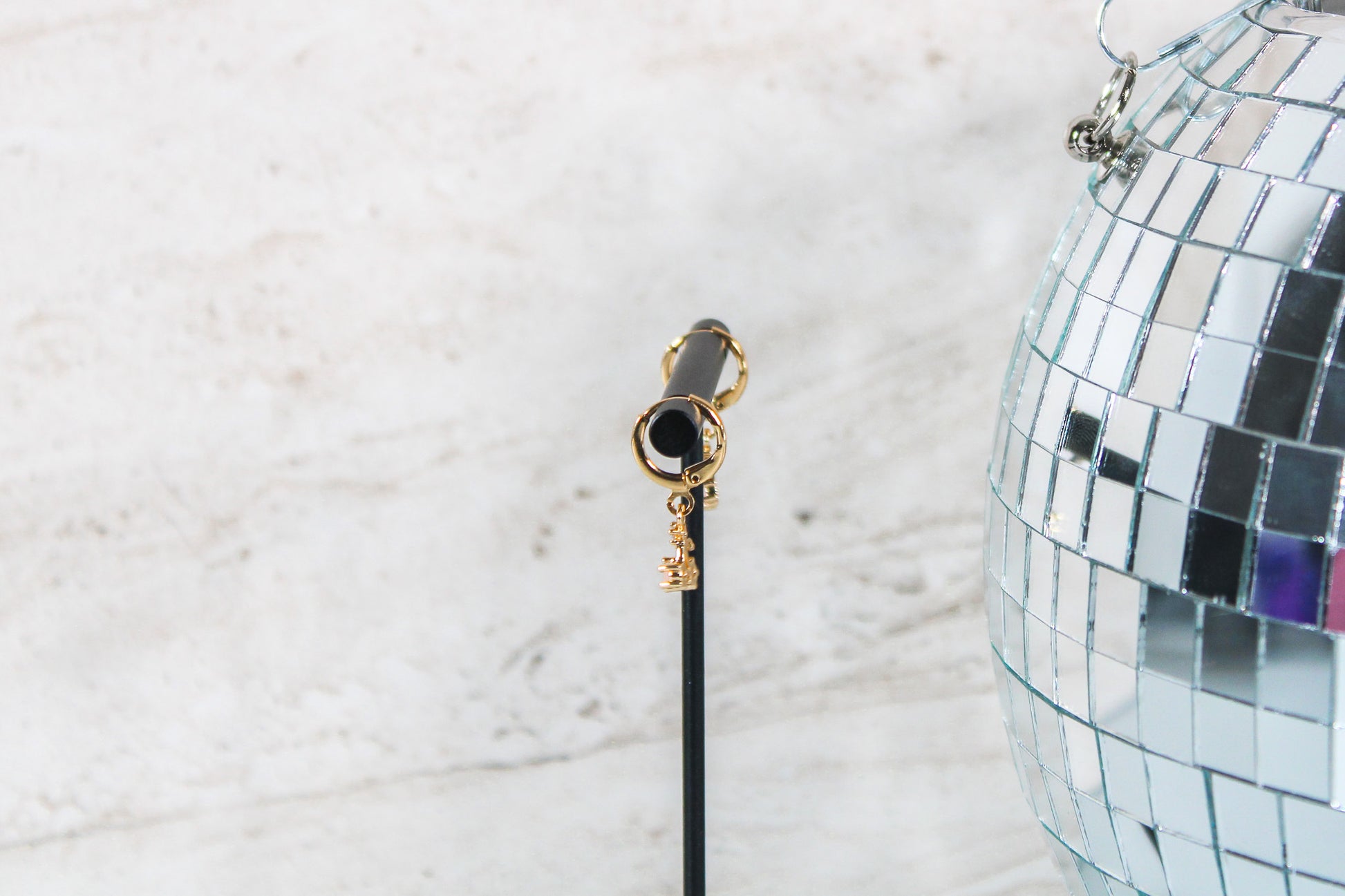 A pair of gold huggie hoop earrings with small cherry charms are displayed on a t bar, showing the side of the earrings.