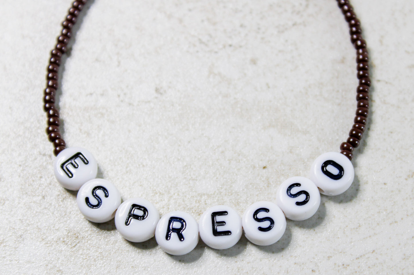 Zoomed-in detail of dark brown beads and center word design.