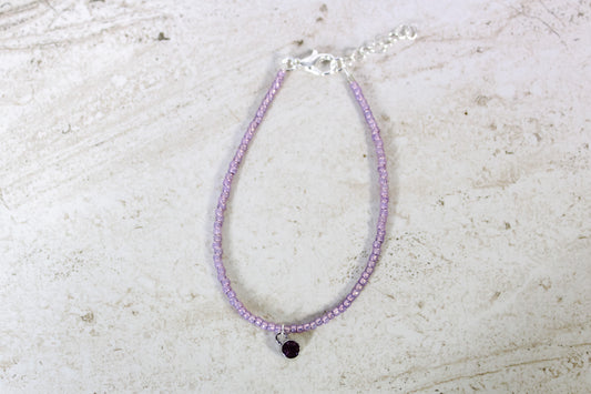 A purple colored seed bead bracelet with a small amethyst silver finished charm and silver lobster clasp and extender chain.