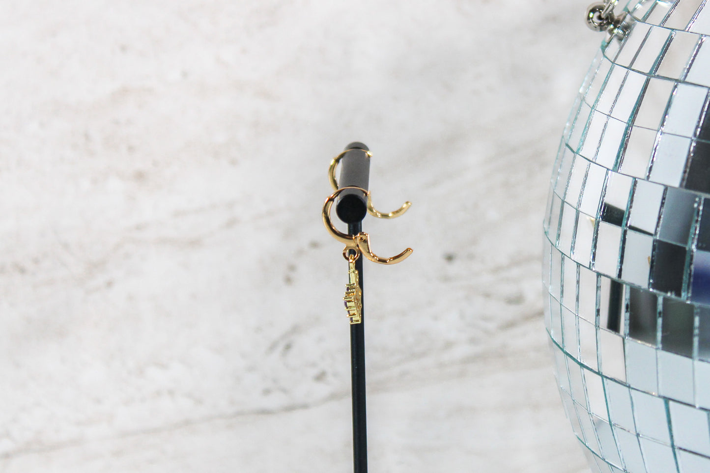 A pair of gold huggie hoop earrings with small grape charms are displayed on a t bar, showing the open clasp of the earrings.