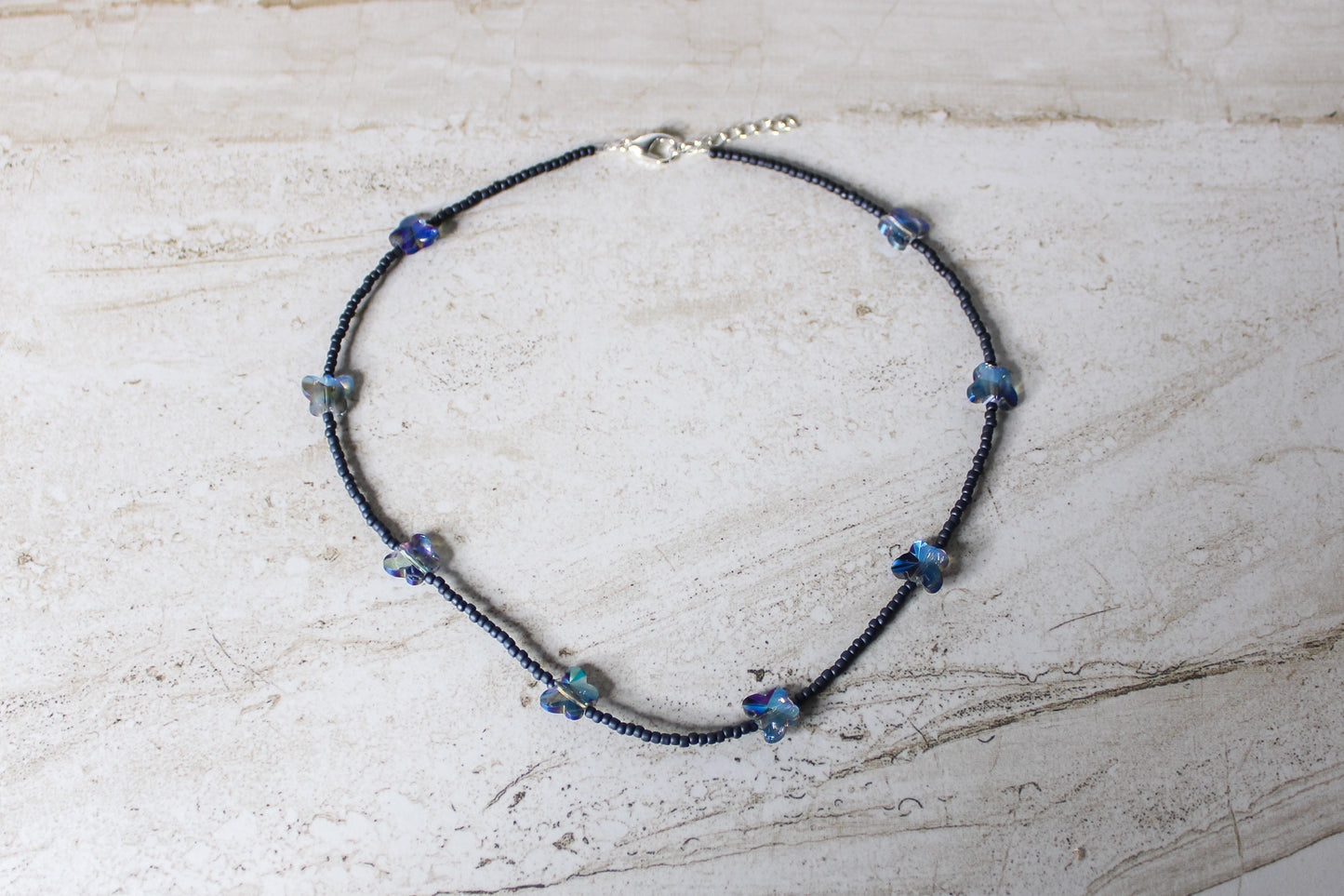 A sleek grey and blue butterfly necklace made with soft glass beads and a whimsical butterfly charm.