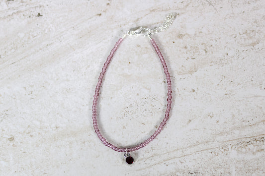 A garnet colored seed bead bracelet with a small garnet silver finished charm and silver lobster clasp and extender chain.