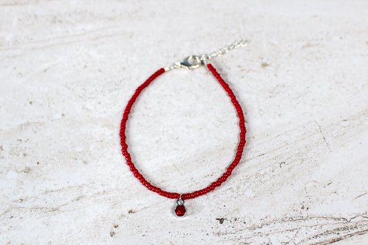 Ruby-inspired July birthstone bracelet with red-toned beads and a silver lobster clasp, displayed flat on a neutral background.