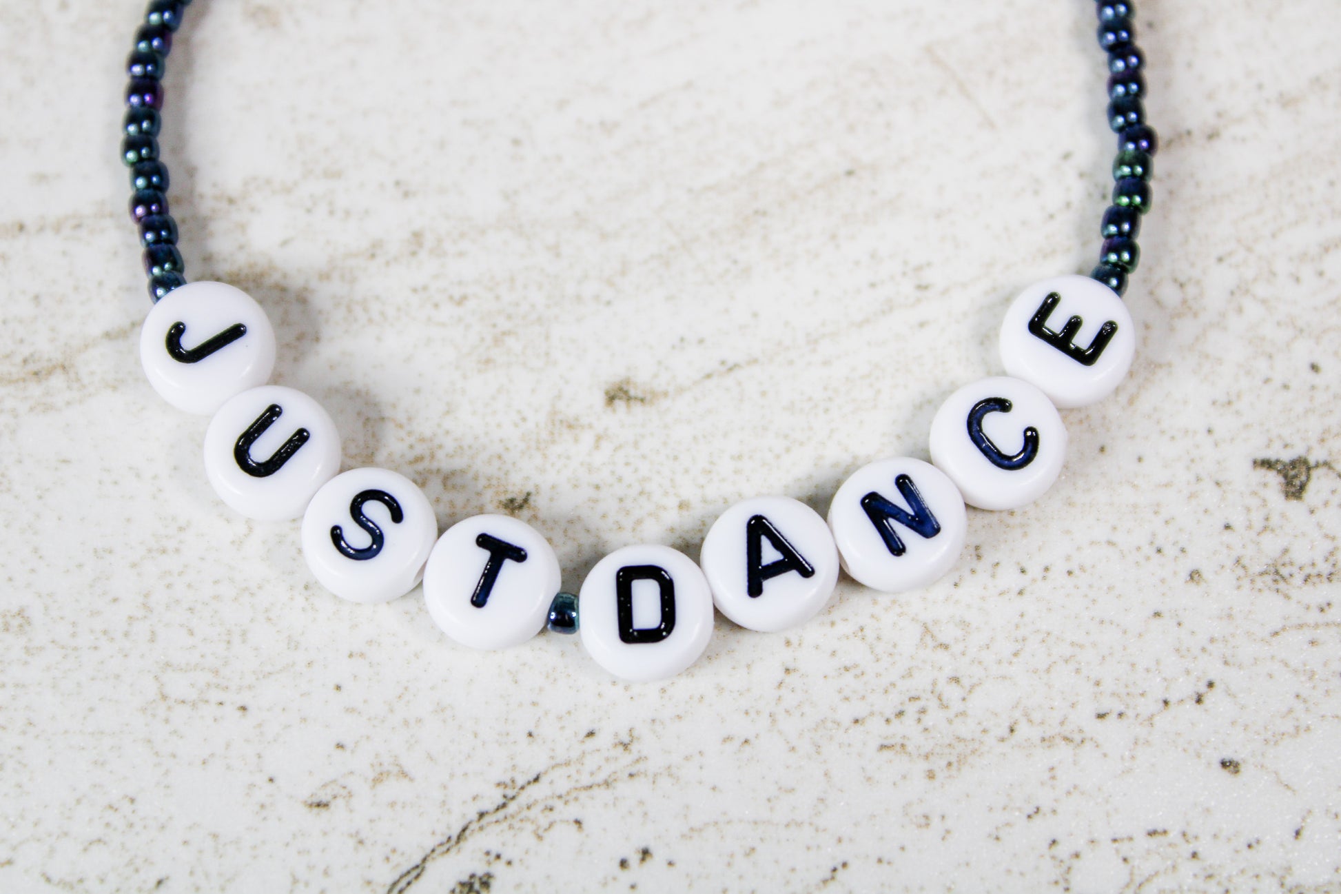 Close-up of the Just Dance phrase spelled out in colorful letter beads surrounded by shimmering oil slick seed beads.