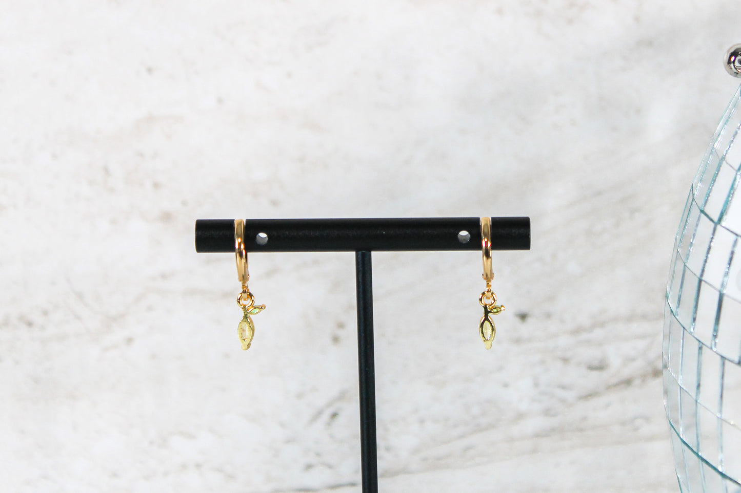 A pair of gold huggie hoop earrings with small lemon cubic zirconia charms are displayed on a t bar, showing the back of the earrings.