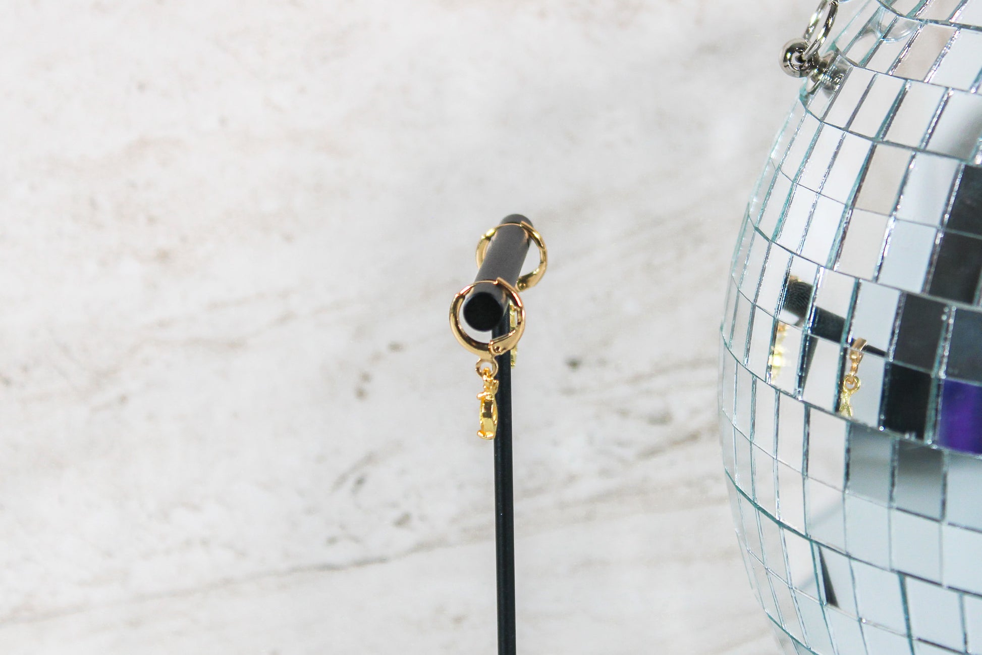 A pair of gold huggie hoop earrings with small lemon charms are displayed on a t bar, showing the side of the earrings.