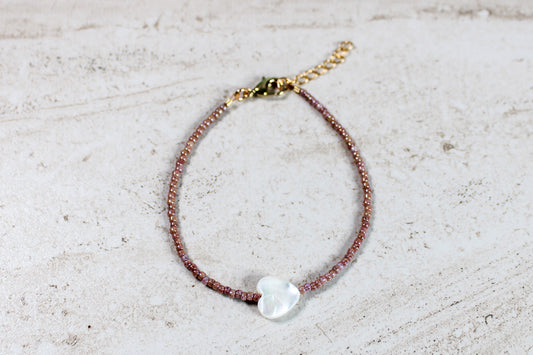 A bracelet made out of marbled pink seed beads with a white shell heart.  Features a gold lobster claw clasp and chain extender.