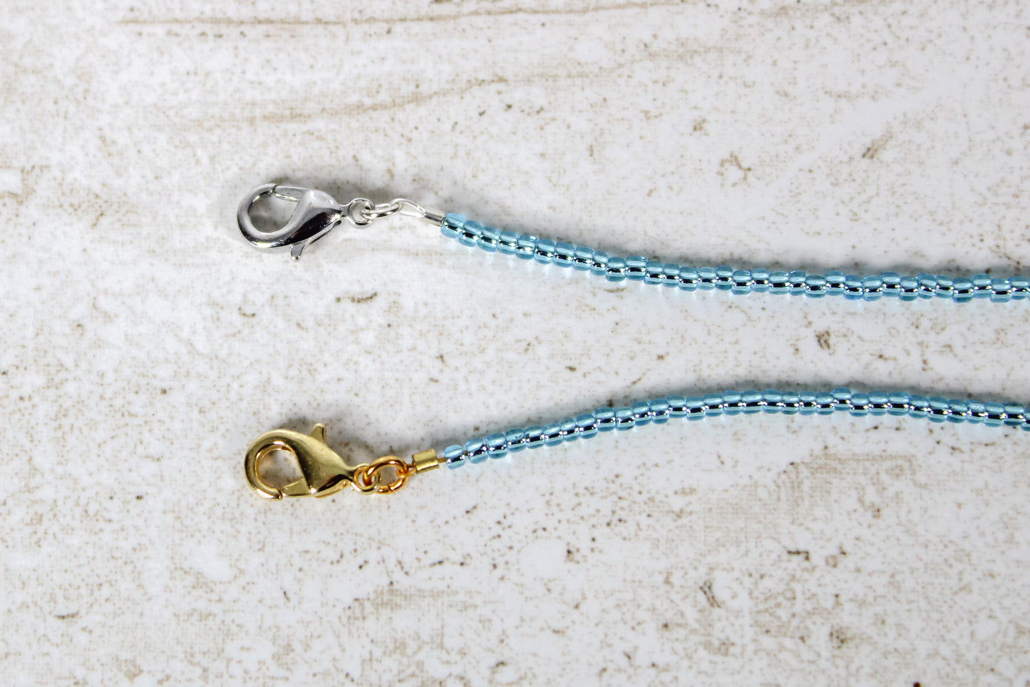 A close up of the gold and silver lobster clasps on an aquamarine bracelet.