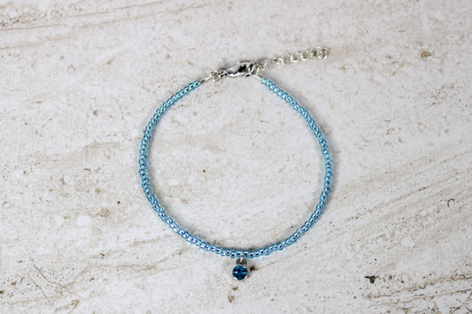 An aquamarine colored seed bead bracelet with a small aquamarine with silver finished charm and silver lobster clasp and extender chain.