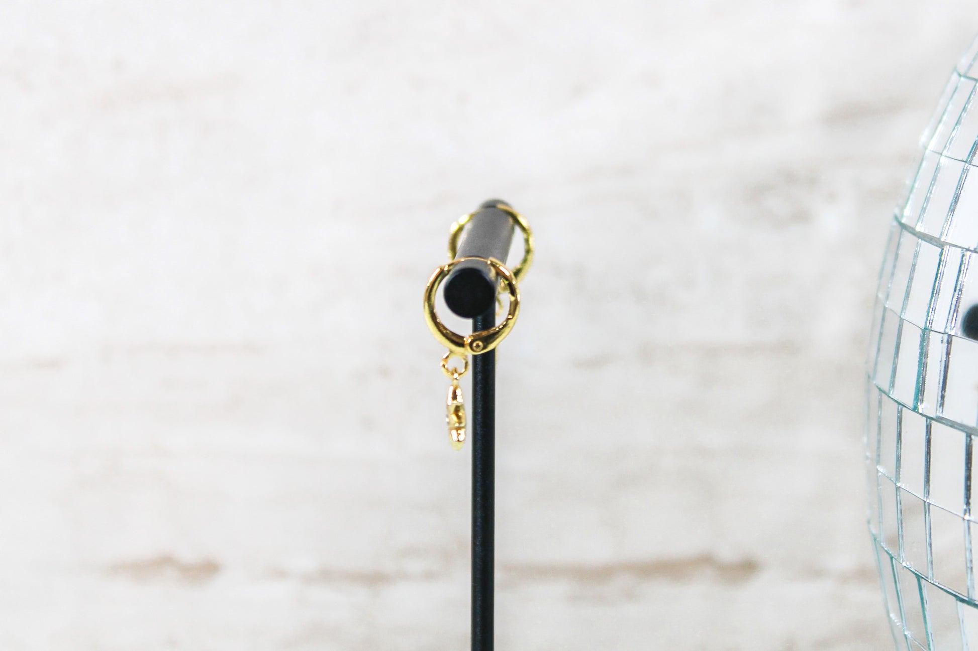A pair of gold huggie hoop earrings with small north star charms are displayed on a t bar, showing the side of the earrings.