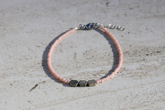 A bracelet made out of matte pale pink seed beads and 3 white gold hexagon charms in the middle.  Features a silver lobster claw clasp and chain extender.