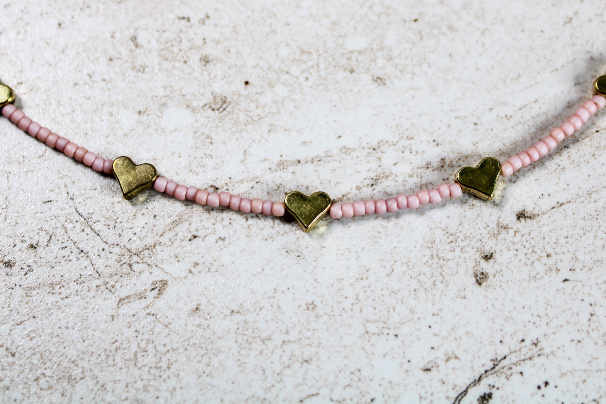 A close up of the pale pink seed beads and gold metal hearts.