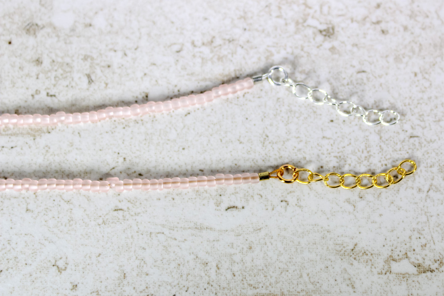 A close up of the gold and silver extender chains on a pale pink bracelet.