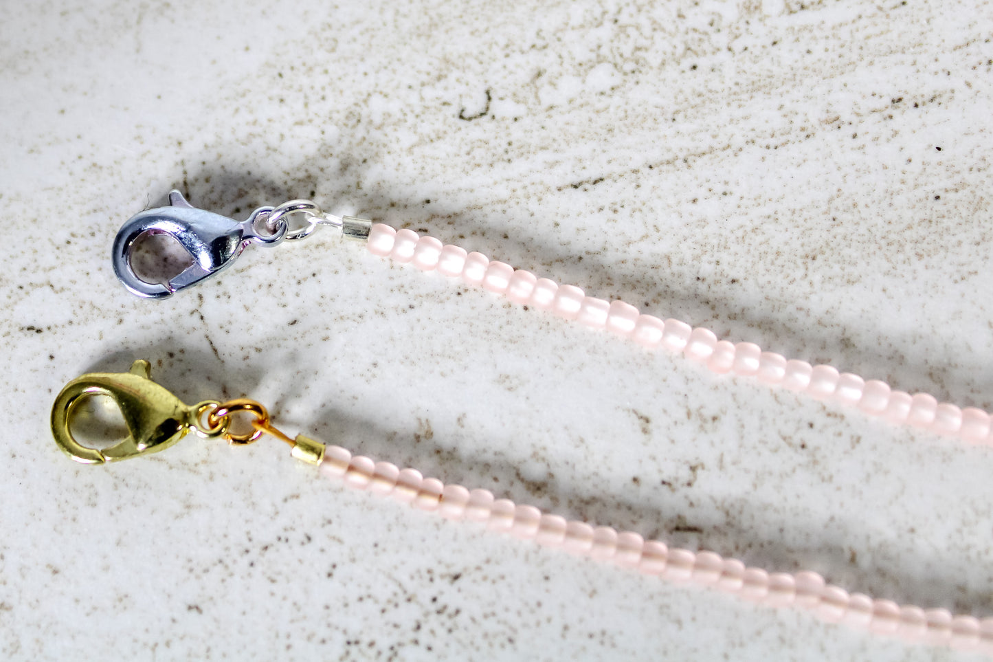 A close up of the gold and silver lobster clasps on a pale pink bracelet.