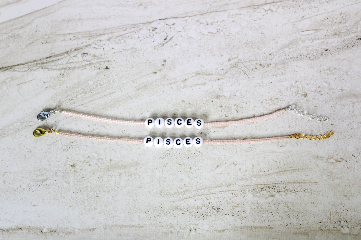 Two bracelets made out of pale pink seed beads with plastic beads that spell out Pisces.