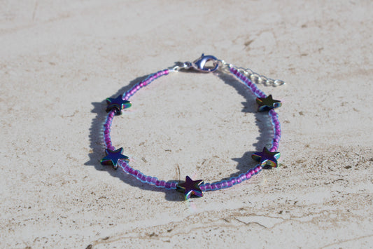 A bracelet made out of purple seed beads and rainbow star charms.  Features a silver lobster claw clasp and chain extender.