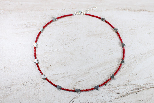 A necklace made out of red seed beads with silver metal hearts spaced evenly throughout.  Features a silver lobster claw clasp and chain extender.