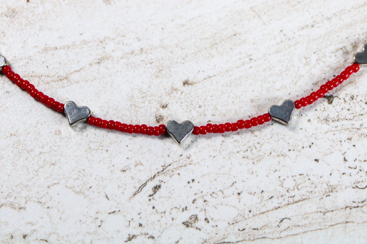 A close up of the red seed beads and silver metal hearts.