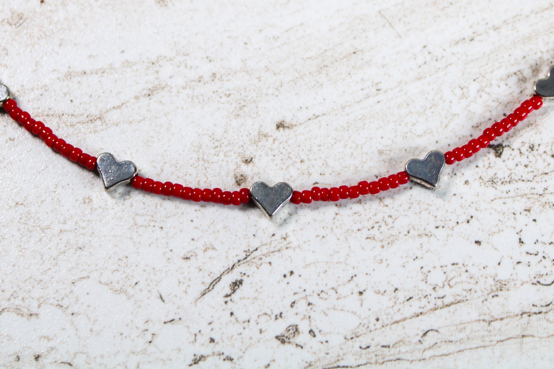 A close up of the red seed beads and silver metal hearts.