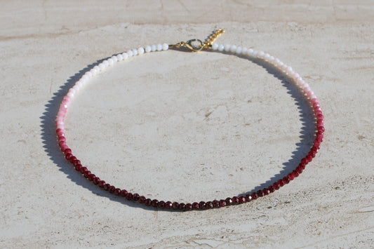 A choker necklace made out of red and white crystal beads.  Features a gold lobster claw clasp and chain extender.