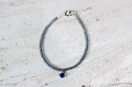 September birthstone bracelet with deep sapphire-colored beads and silver hardware, displayed on a minimal backdrop.