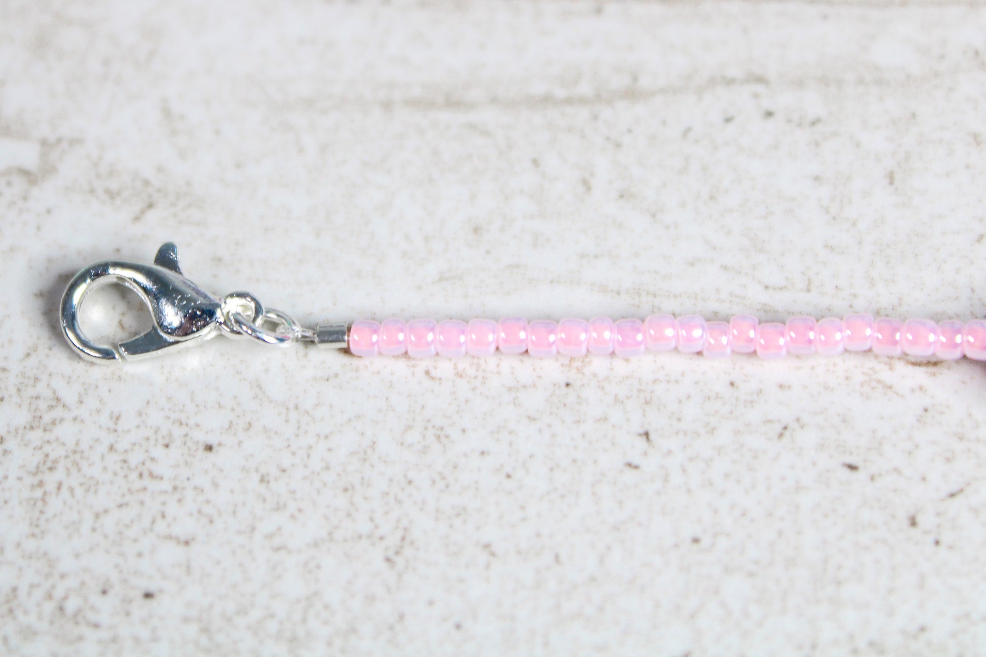 Zoomed-in view of the silver lobster claw clasp at the end of the light pink beaded bracelet

