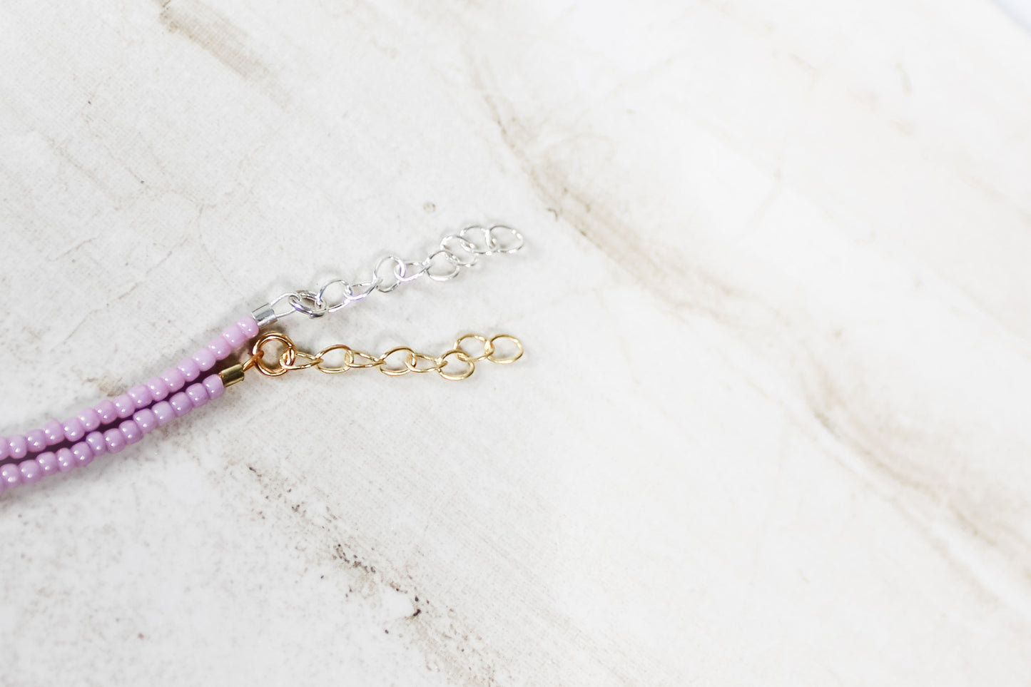 A close up of the gold and silver extender chains on a shiny mauve bracelet.