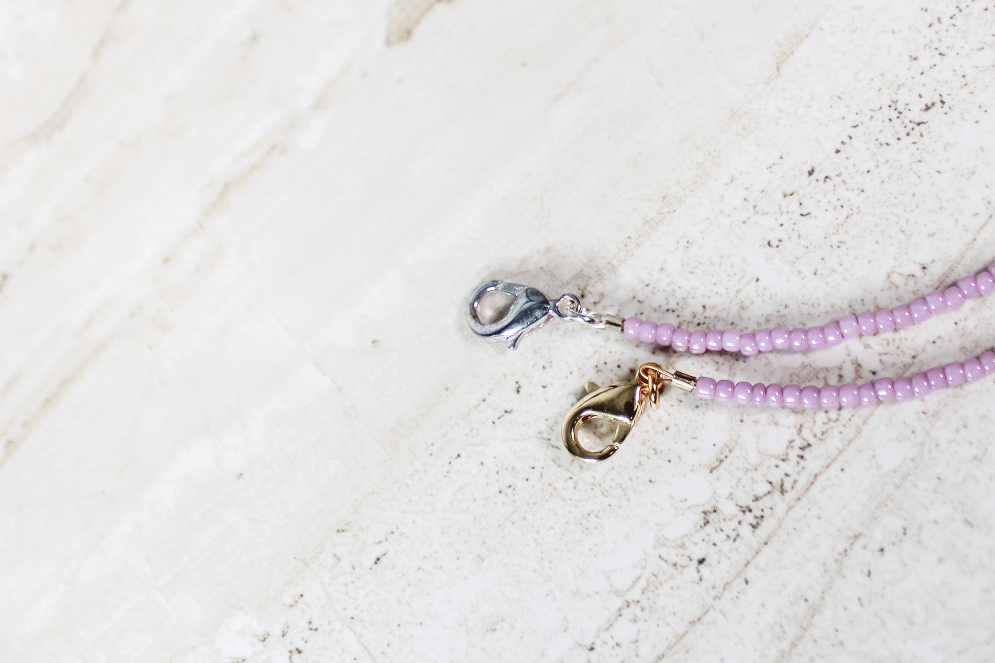 A close up of the gold and silver lobster clasps on a shiny mauve bracelet.